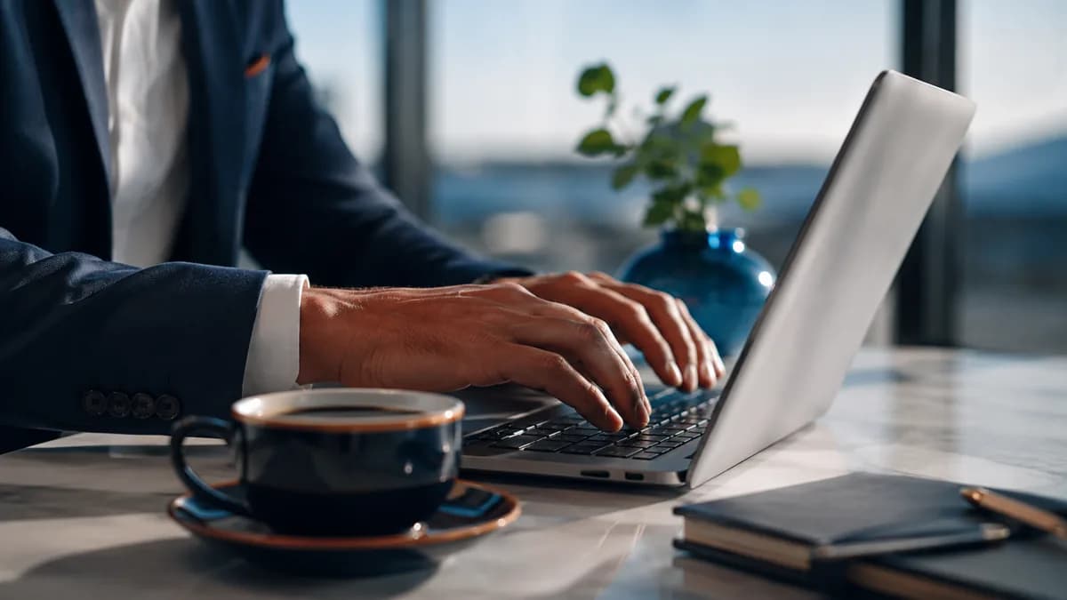 Mani su una tastiera del computer con una tazza di caffè, che illustra la redazione di un modello di email di rimborso